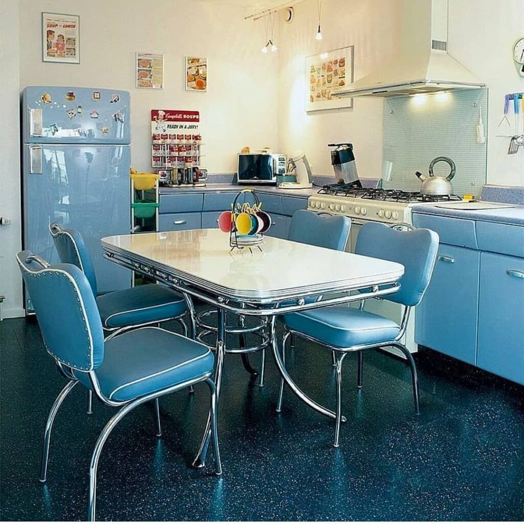 Blue retro kitchen with blue diner chairs, a chrome table, dark blue floor, and a vintage-style blue refrigerator.